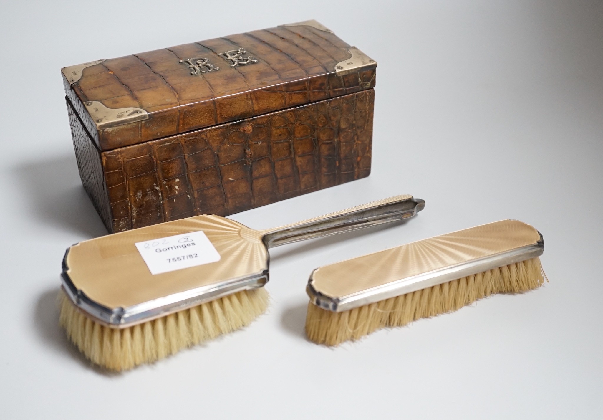 A late Victorian silver mounted crocodile skin jewellery box, 19cm and two silver and enamel mounted brushes.